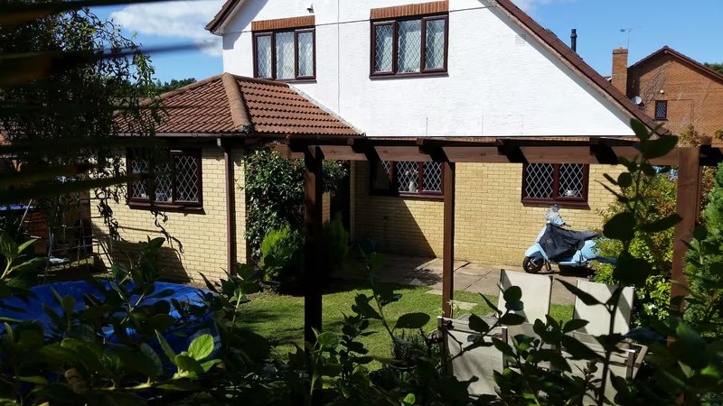 Brick and white rendered house exterior with pergola, garden, and blue parasol