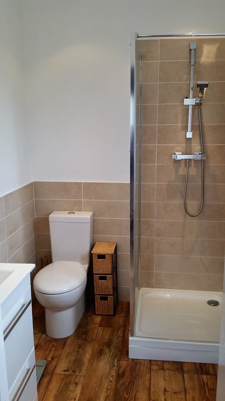 Bathroom with toilet, shower enclosure, wooden floor and beige tile walls
