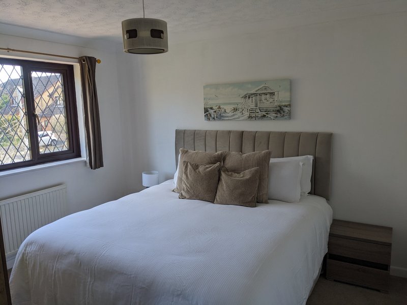Bedroom with double bed, grey upholstered headboard, white bedding, and leaded-glass window