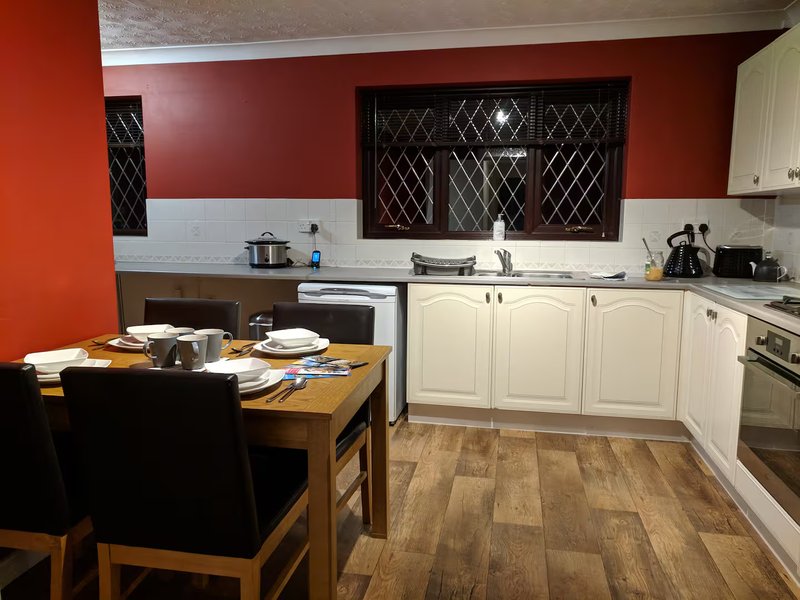 Kitchen and dining area with cream cabinets, red accent wall, wooden table and black chairs