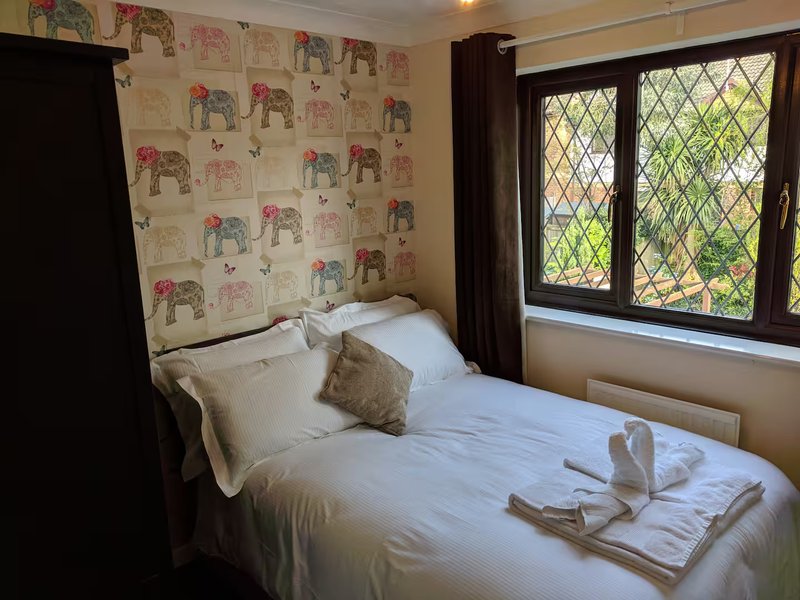 Bedroom with single bed, elephant-patterned wallpaper, leaded windows and dark wooden frame