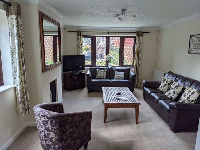 Spacious living room with leather sofas, patterned armchair, coffee table and large windows