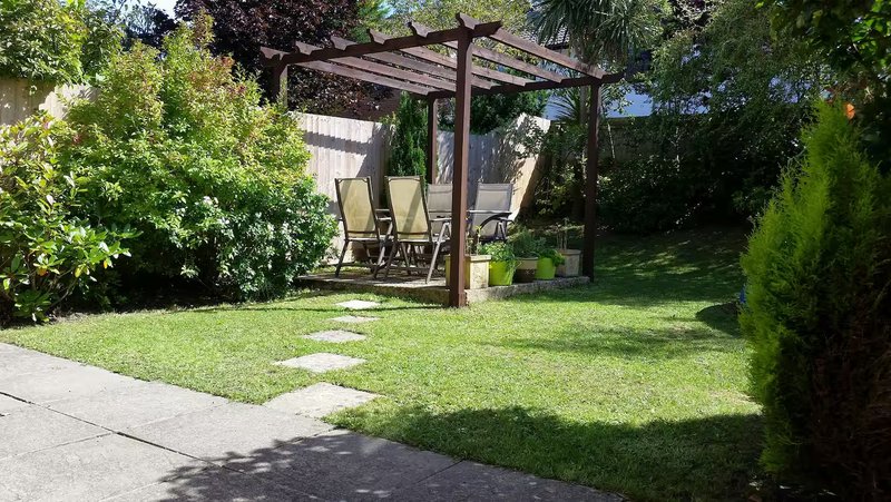 Garden with pergola, lawn, seating area, and planted borders on sunny day