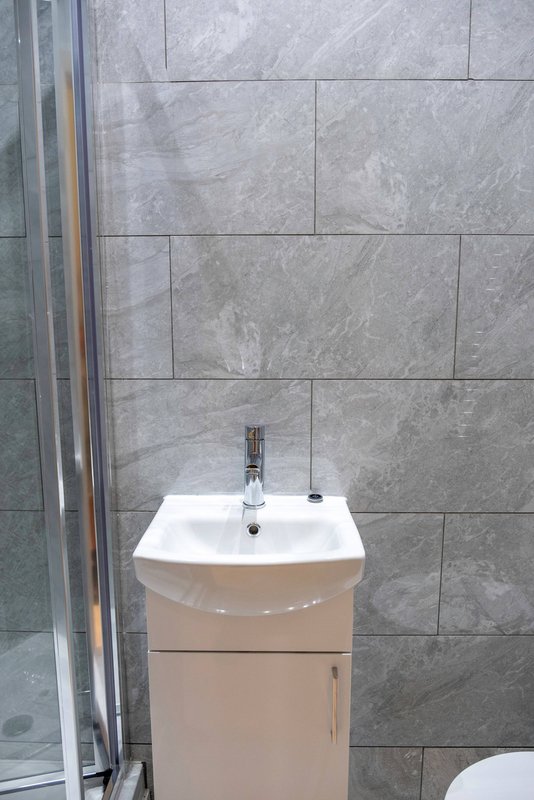 Modern bathroom with white vanity sink, grey tiled walls and glass shower enclosure