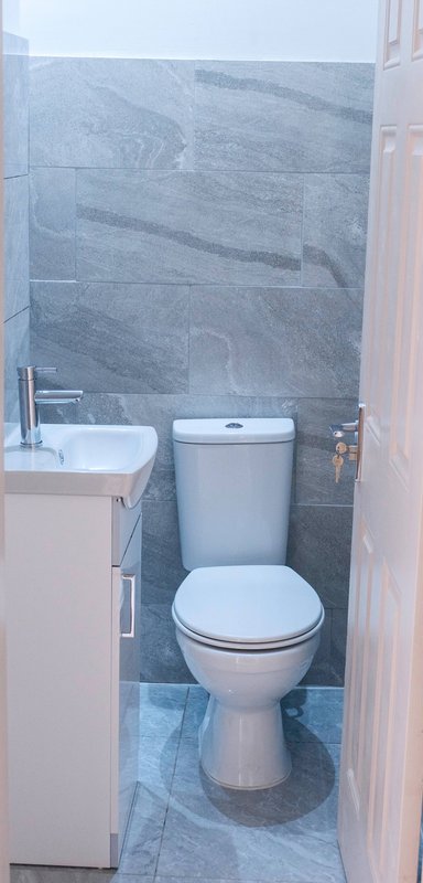 Compact bathroom with toilet, small sink, and blue-grey tile walls