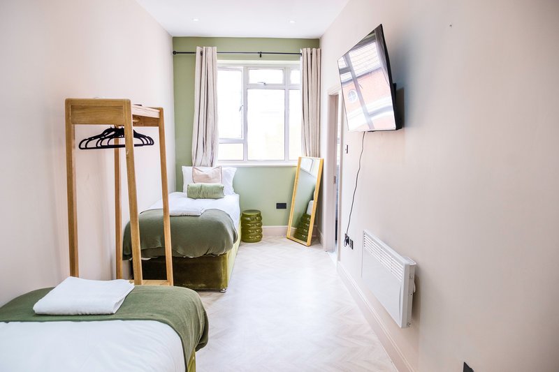 Compact bedroom with two single beds, wooden coat rack, wall-mounted TV and bright window