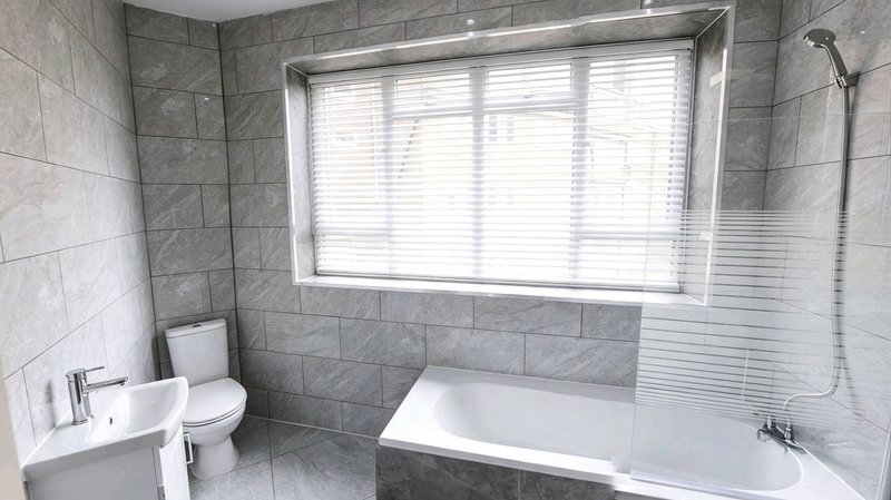 Modern bathroom with grey tile walls, white suite, bathtub and large window