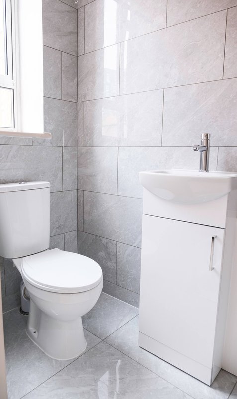 Modern bathroom with white toilet, pedestal sink, grey tile walls and window