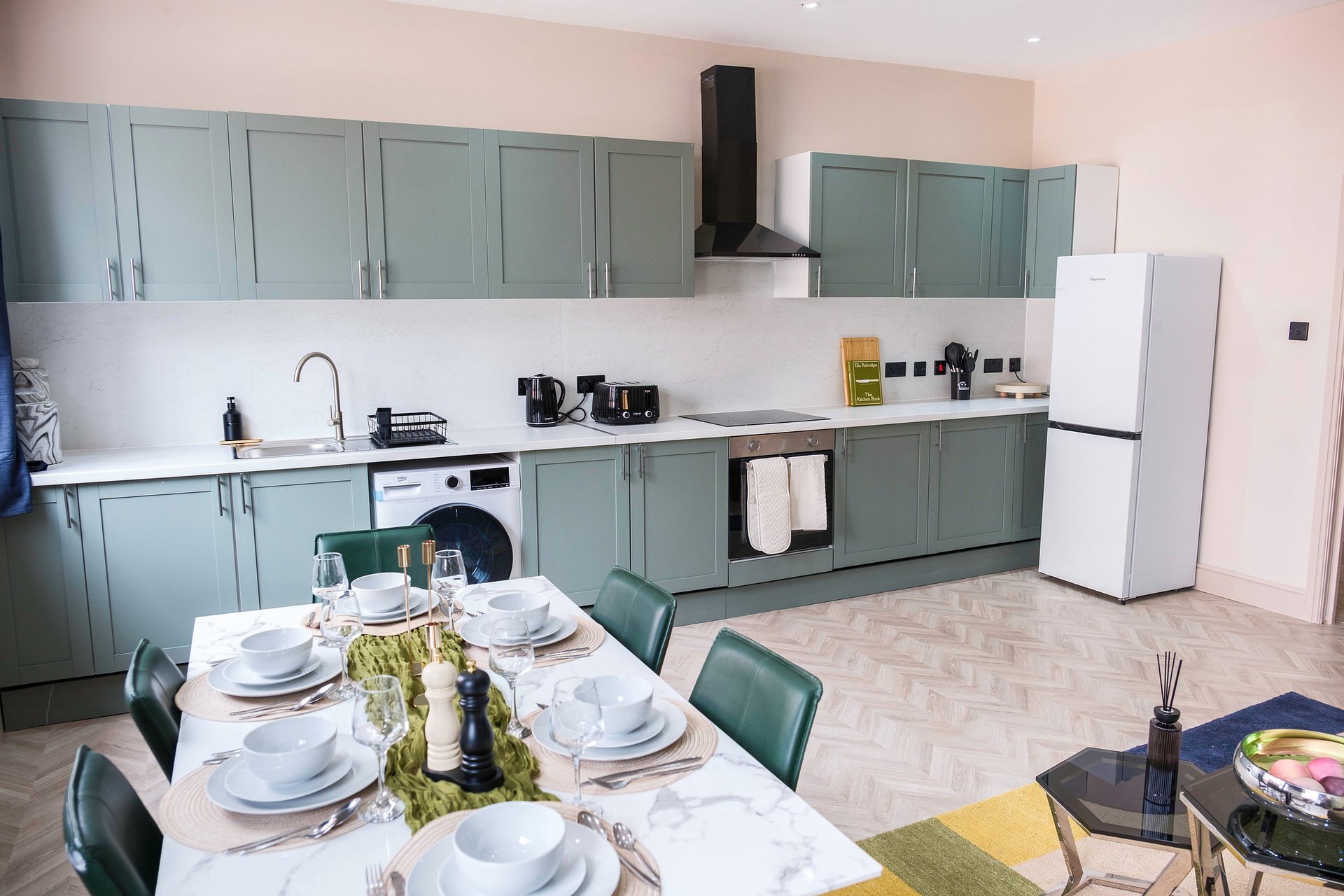 Modern kitchen with sage green cabinetry, white countertops, and dining table set for a meal