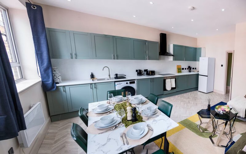 Modern open-plan kitchen and dining area with teal cabinetry, white countertops, and dining table set for two