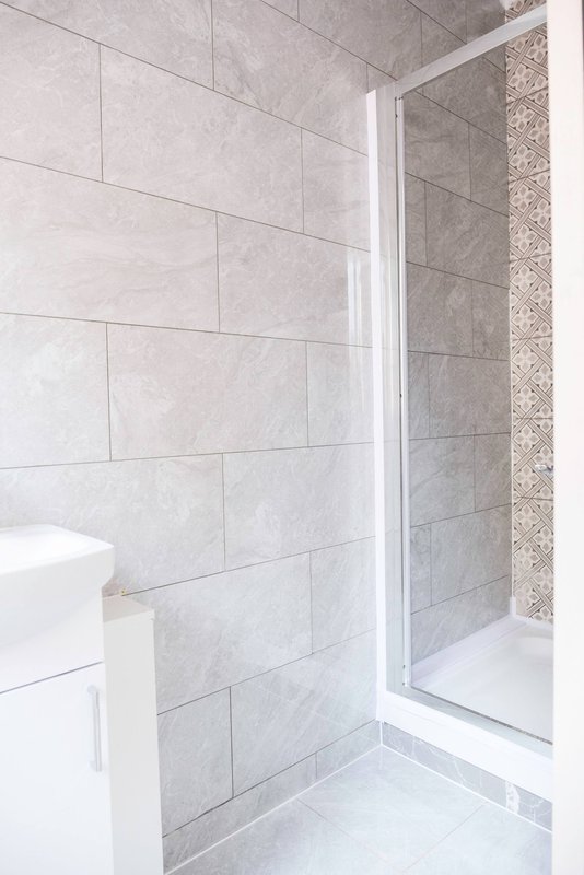 Modern bathroom with gray tile walls, white toilet, and glass shower enclosure