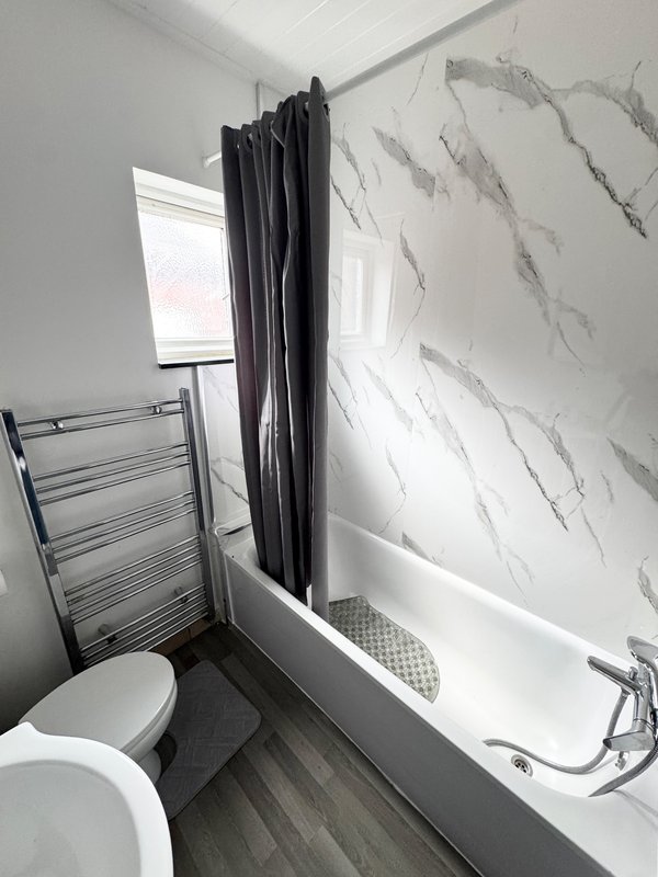 Modern bathroom with white bathtub, black shower curtain, toilet and heated towel rail