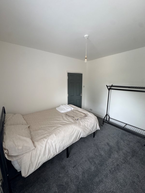 Bedroom with bed, white bedding, dark door, clothes rack, and pendant light