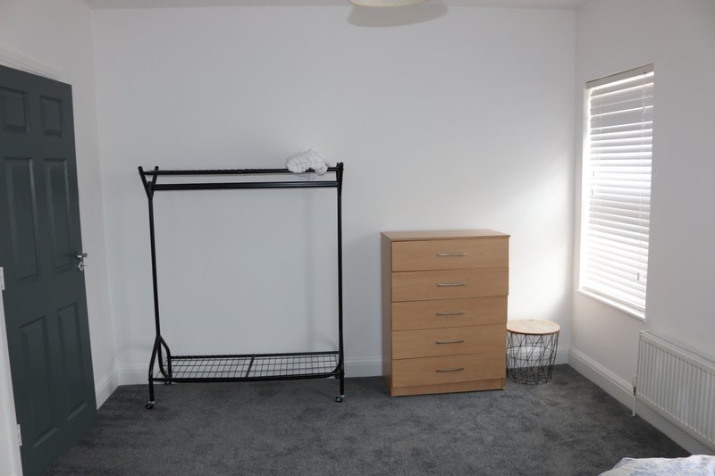 Bedroom with metal clothing rack, wooden chest of drawers, and dark carpet flooring