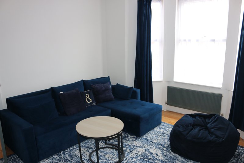 Modern living room with blue corner sofa, round white table, bean bag chair and large windows