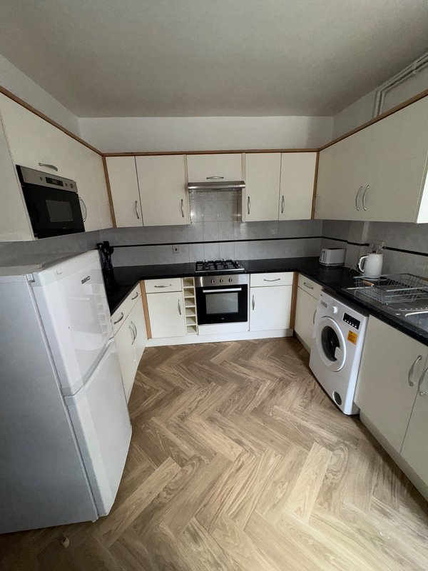 Modern kitchen with cream cabinets, black countertops, integrated appliances and herringbone flooring