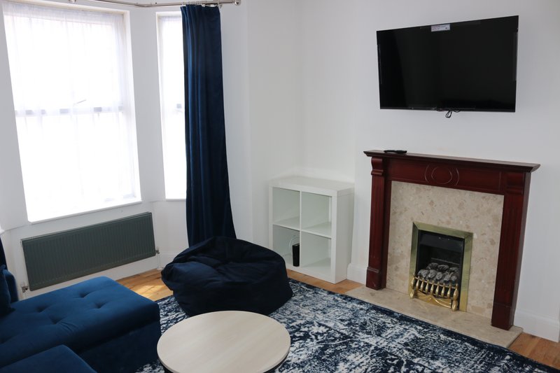 Living room with blue sofa, fireplace, wall-mounted TV, and large window with blue curtains