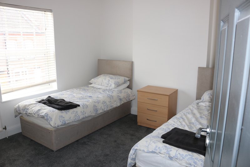 Shared bedroom with two single beds, wooden bedside table, and large window with blinds