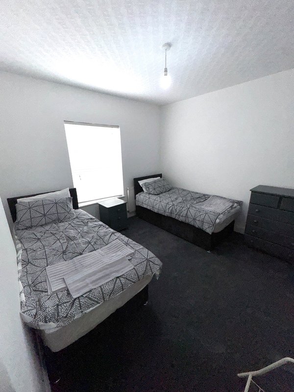 Shared bedroom with two single beds, dark flooring, white walls and window