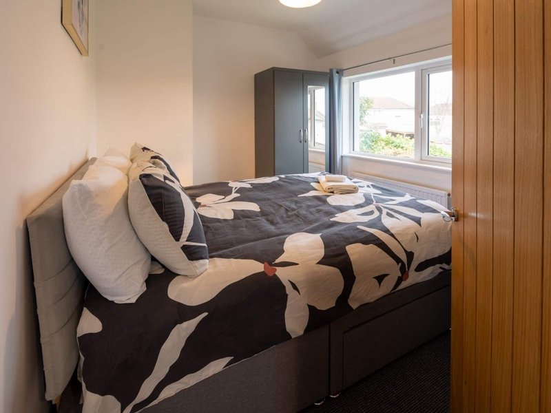 Bedroom with double bed, patterned duvet, pillows, wooden wardrobe and window with garden view