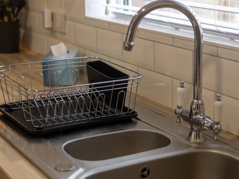 Kitchen sink with chrome faucet, dish rack, and subway tile backsplash