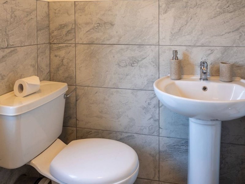 Bathroom with toilet, pedestal sink, marble tile walls and toiletries