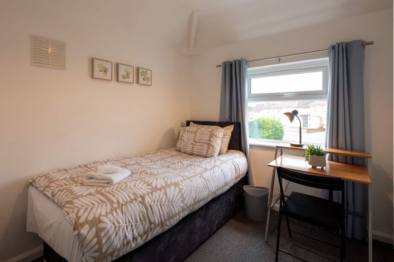 Bedroom with single bed, wooden desk, chair and window with grey curtains