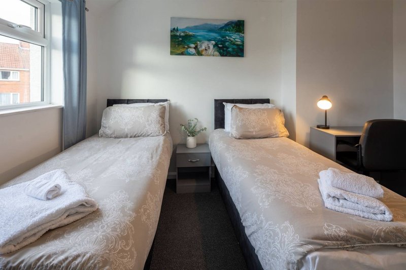 Twin bedroom with two single beds, bedside table, landscape artwork and window with curtains