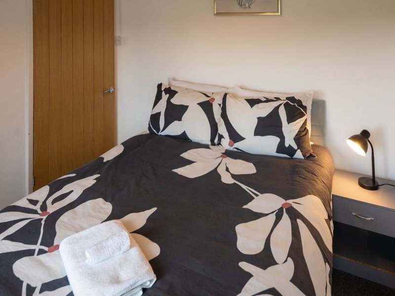 Bedroom with double bed, black and white patterned bedding, wooden door, and bedside lamp