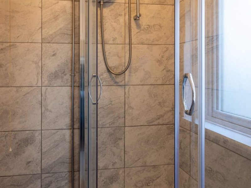 Bathroom shower enclosure with tiled walls, glass doors and chrome fixtures