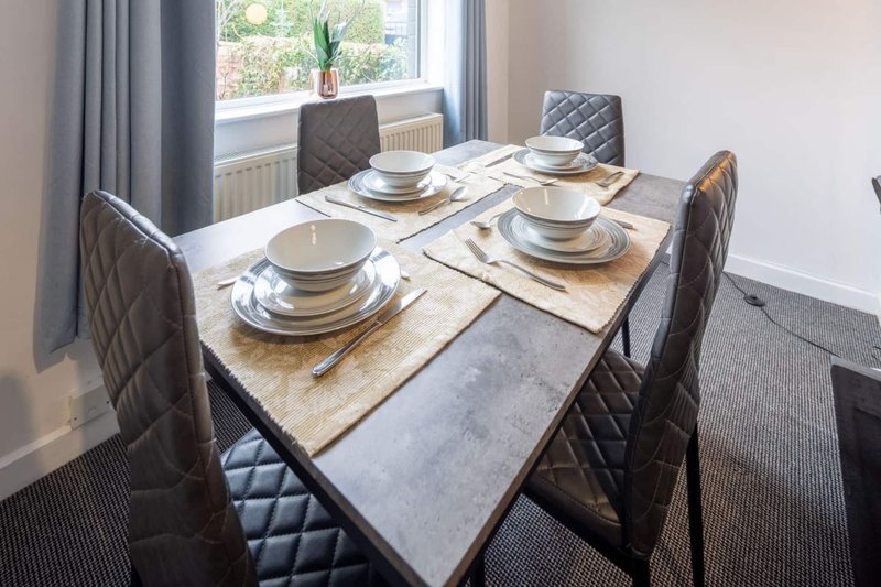 Dining table set for four with place settings, chairs, and window view