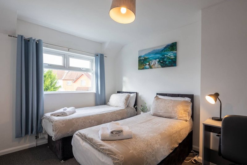 Twin bedroom with two single beds, wooden bedside tables, ceiling light and window with blue curtains
