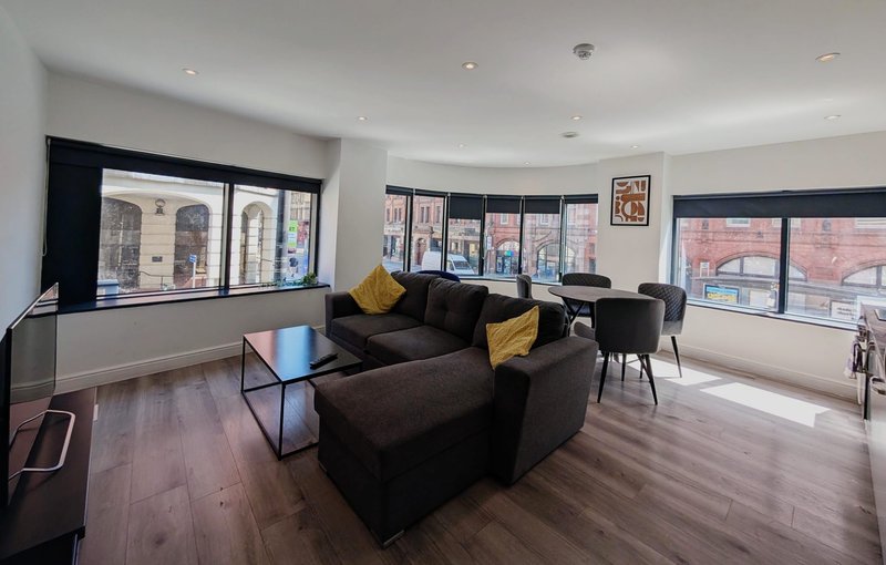 Spacious open-plan living area with black sofas, yellow cushions, wooden flooring and large windows