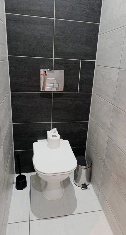 Small bathroom with white toilet, black and gray tile walls, waste bin and toilet brush