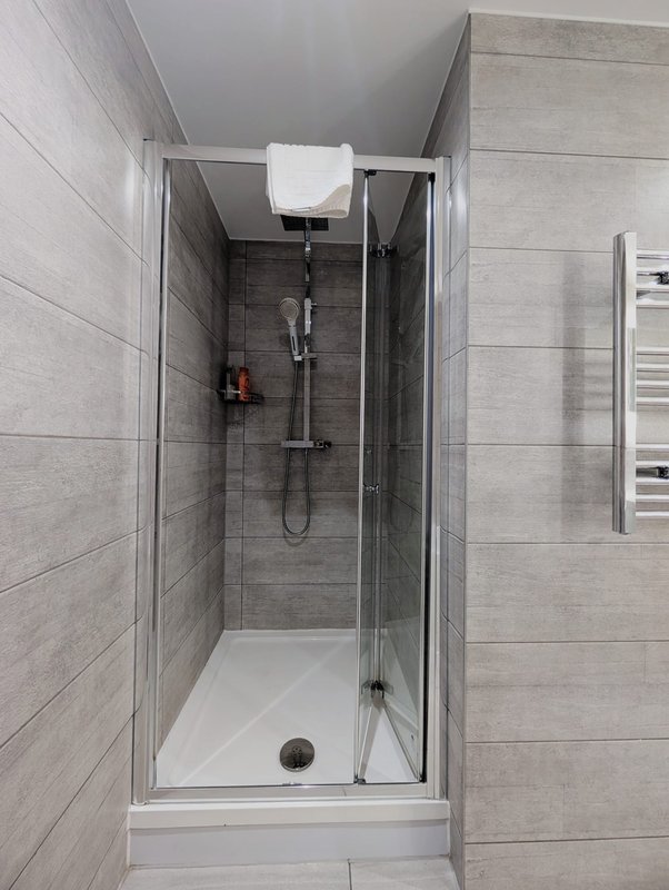 Modern ensuite shower cubicle with grey tile walls, glass door, and chrome fixtures