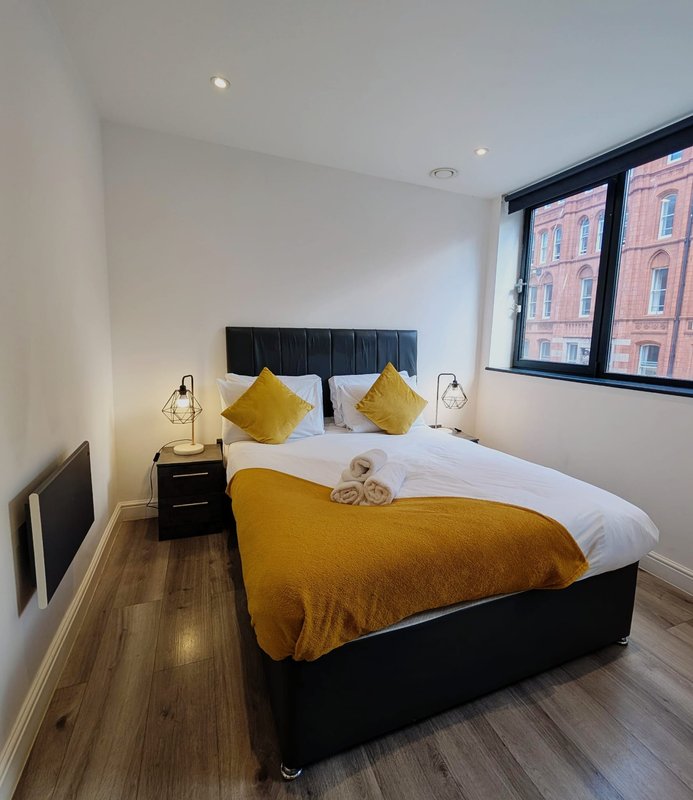 Modern bedroom with black bed, yellow throw and cushions, bedside lamps, wooden floor