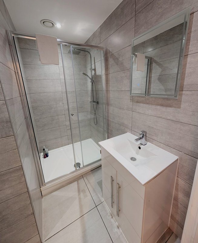 Modern bathroom with walk-in shower, white vanity sink, and grey tile walls