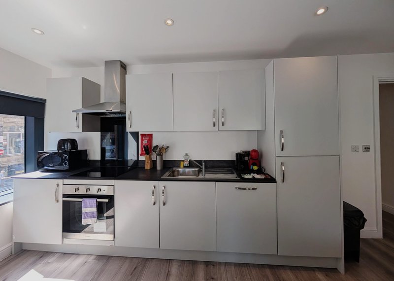 Modern kitchen with white cabinetry, black countertop, integrated appliances and breakfast bar