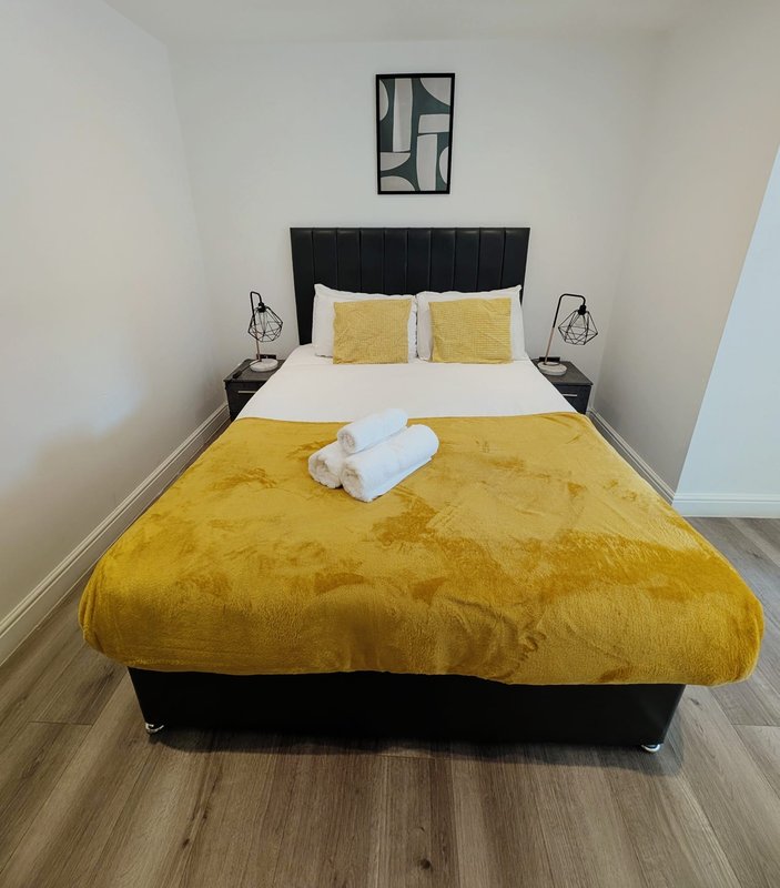 Bedroom with double bed, yellow bedding, black headboard, and wall art