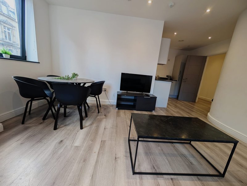 Open-plan apartment interior with dining table, TV stand, coffee table and kitchen area
