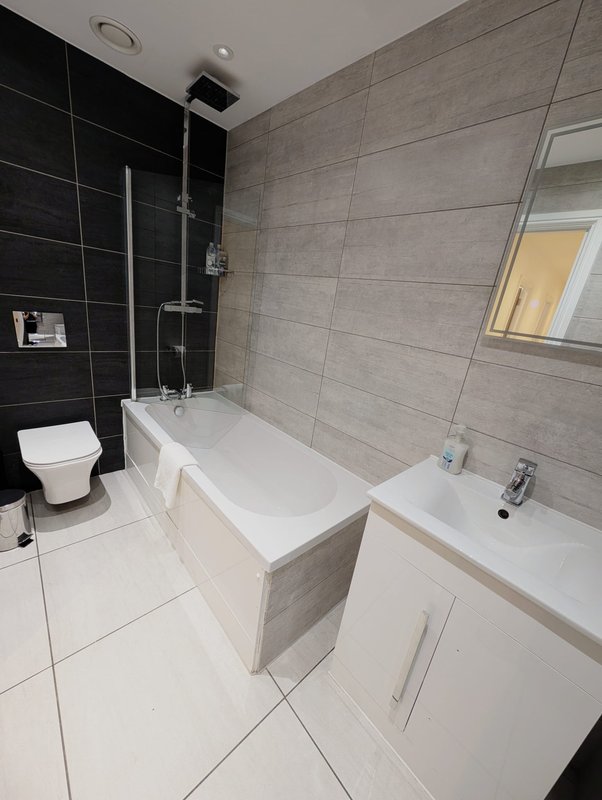 Modern bathroom with white bathtub, dual sink vanity, black tile shower area and toilet