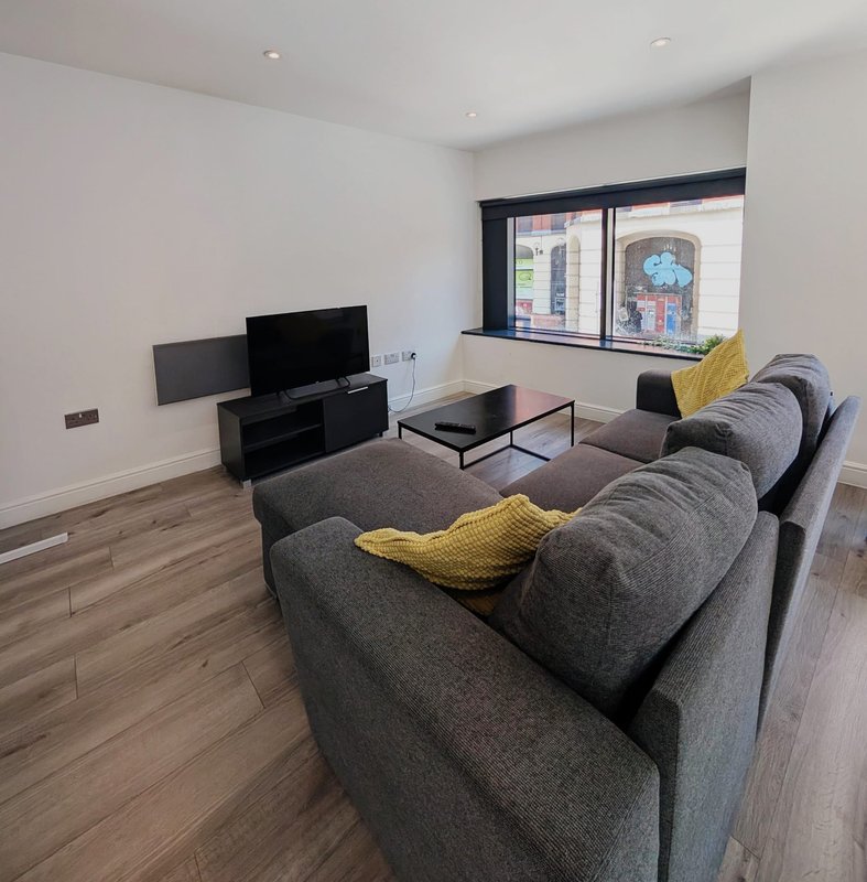 Modern living room with gray upholstered sofa, TV on stand, coffee table, yellow cushions and wooden flooring