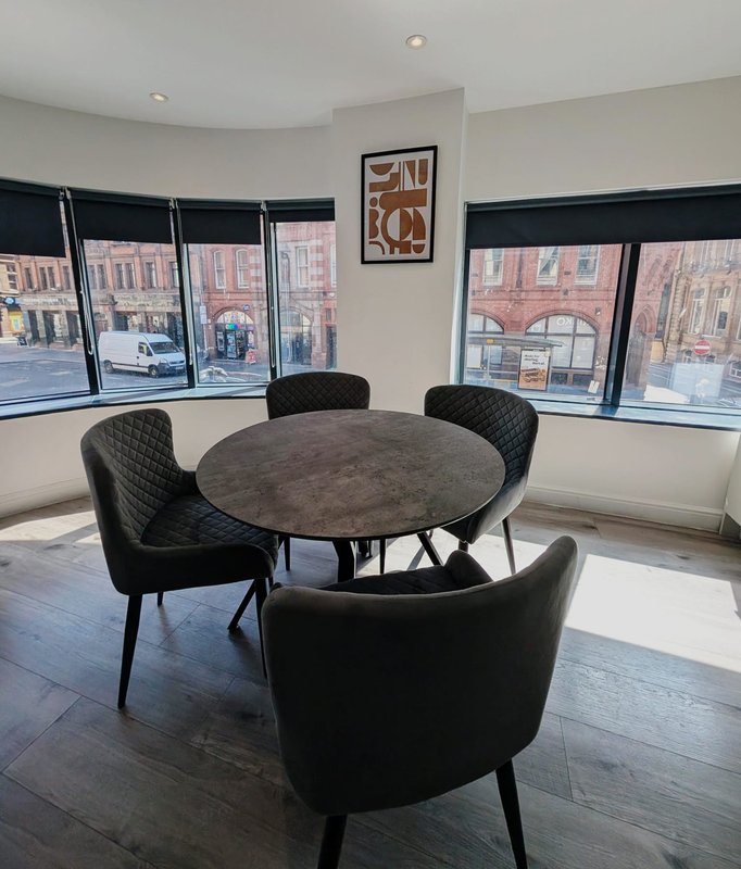Modern dining area with round dark table, black upholstered chairs, large windows overlooking street