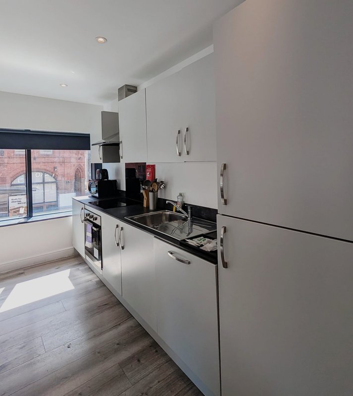 Modern white kitchen with black countertop, appliances, and brick building view through window