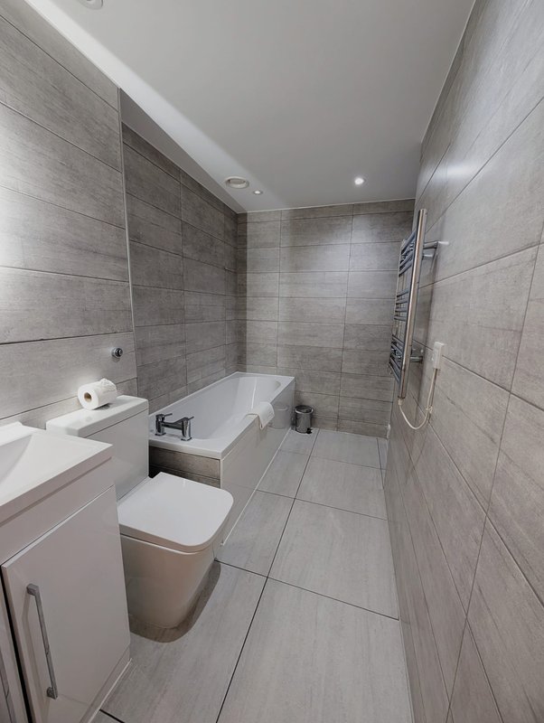 Modern bathroom with grey tile walls, toilet, sink vanity, and bathtub with shower enclosure