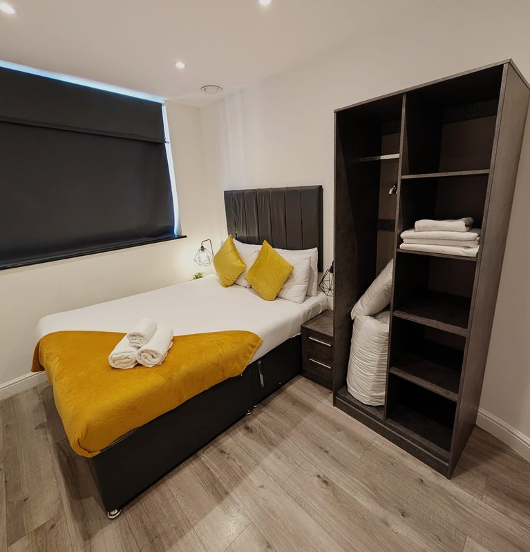 Modern bedroom with double bed, yellow bedding, black headboard and open wardrobe storage