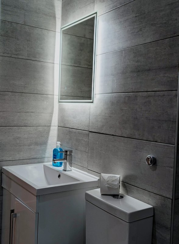 Modern bathroom with gray tile walls, illuminated mirror, white sink and toilet