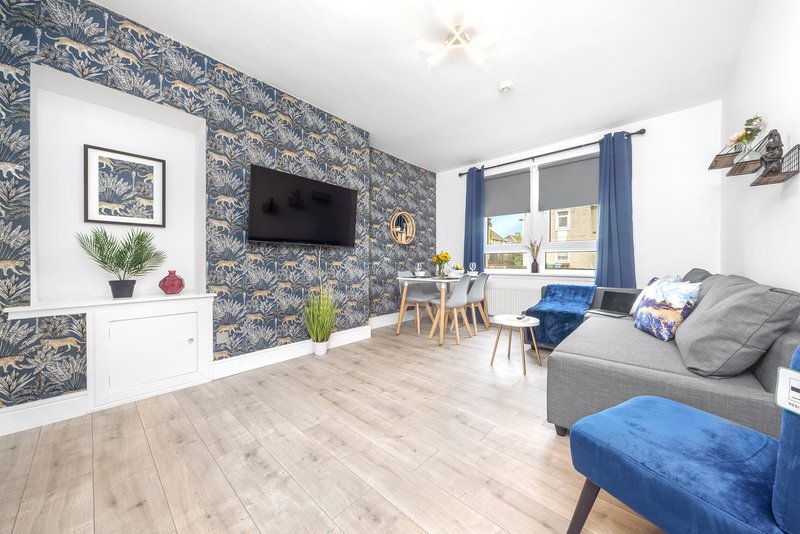 Modern living room with patterned wallpaper, gray sofa, blue accents, and wooden flooring