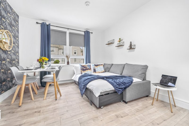 Modern studio bedroom with grey sofa bed, desk, dining table and window with blue curtains