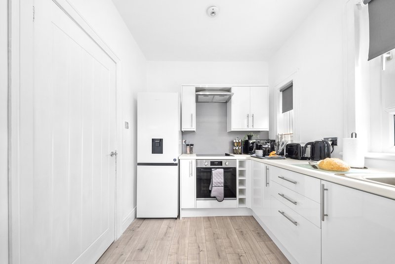 Modern white kitchen with appliances, wooden flooring, and compact layout